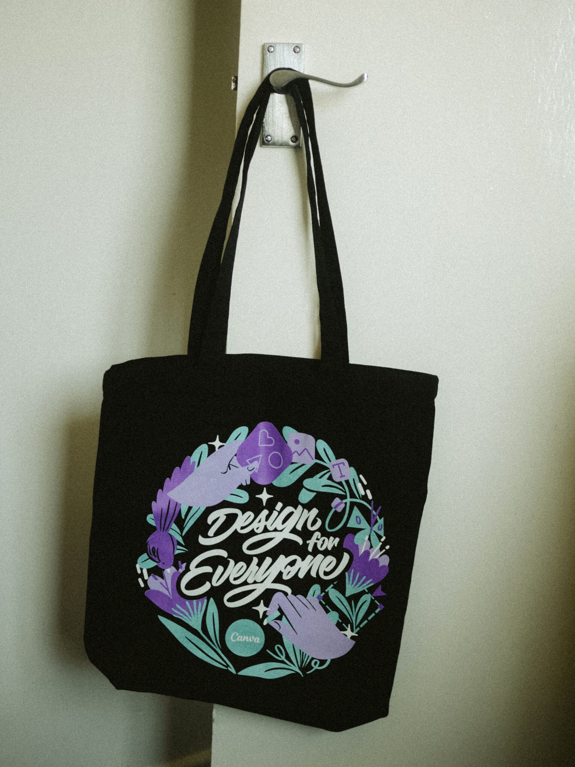 A stylish black tote bag with a floral design hanging on a door hook indoors.